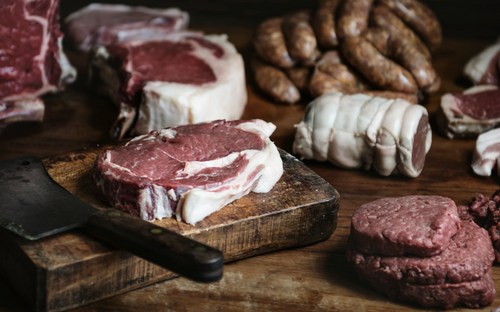 Selection of raw meat cuts, including steaks, sausages and mince on a wooden board.